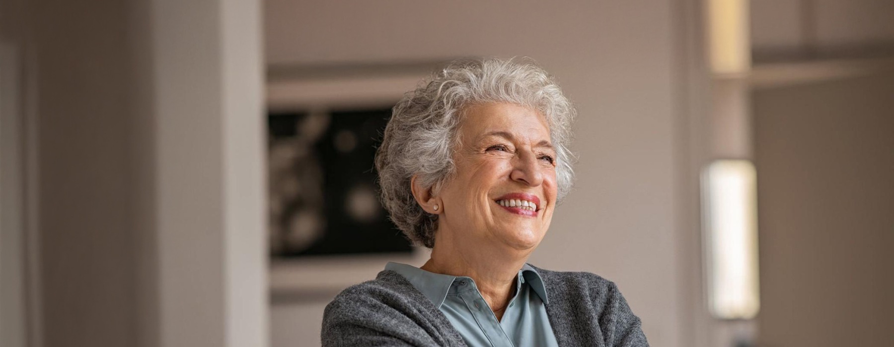 elderly woman with a cane, sits in a room and smiles